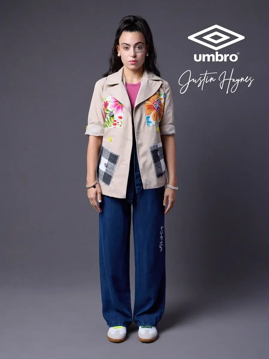 Lookbook photography for the Umbro France collection. Vanessa standing front-facing in a sand utility jacket with floral patchwork panels over a fuchsia t-shirt and wide-leg dark indigo jeans, styled by Justin Haynes, photographed in Springfield, Mas