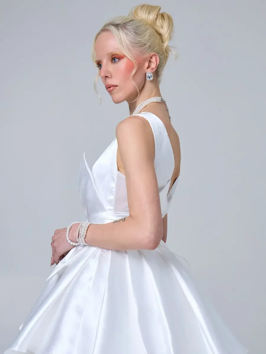 JUS10H 2025 New York Bridal Fashion Week, white satin ball gown with deep open back and V-neckline, styled with layered pearl choker, pearl bracelet, and crystal drop earrings, photographed by Scott Parker Photo