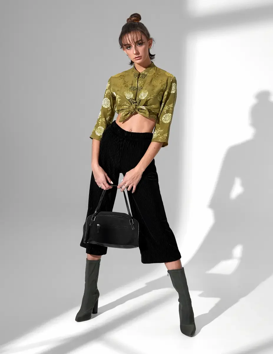 Model Macy, full length, olive green satin jacquard tied crop top with gold medallion print and frog closures, black wide-leg ribbed velvet culottes, olive green block-heel sock boots, black suede barrel bag, New York studio test shoot, photographed 