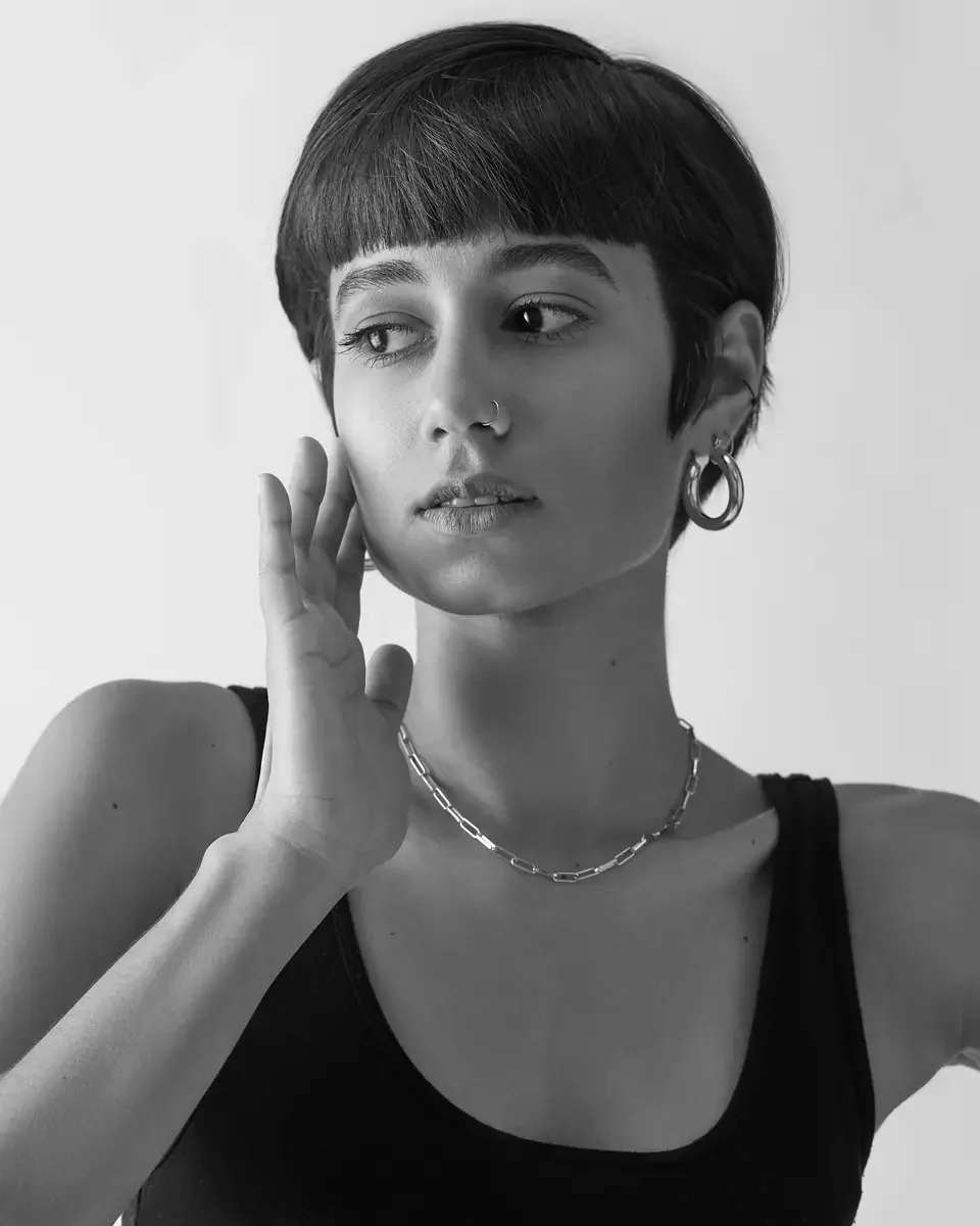 Eloissa, black and white portrait, hand raised, gold hoop earring, nose ring, chain necklace, blunt fringe pixie cut, East Williamsburg studio test shoot, makeup by Schanica Pickens, photographed by Scott Parker Photo