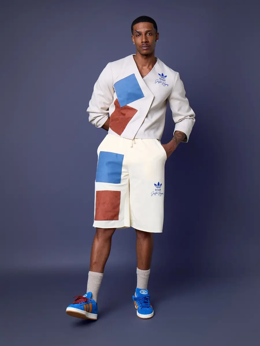 JUS10H x Adidas Brasil campaign, full-length standing shot, white patchwork wrap long-sleeve top with blue and terracotta suede panels over cream patchwork shorts, Adidas Campus 00s in royal blue suede with orange stripes, periwinkle background, phot
