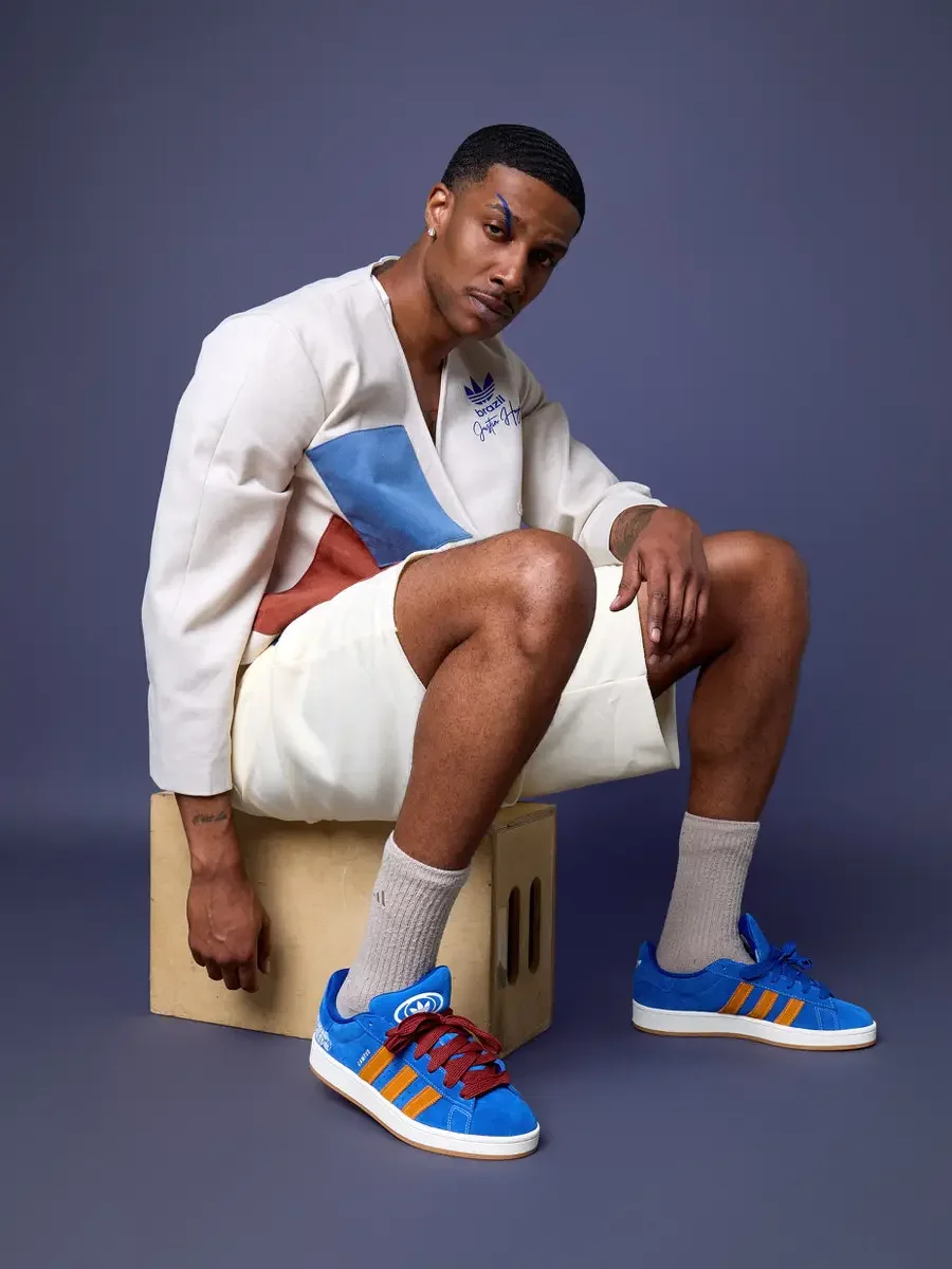 JUS10H x Adidas Brasil campaign, model seated on wood block, white patchwork wrap long-sleeve top with blue and terracotta suede panels over cream patchwork shorts, Adidas Campus 00s in royal blue suede with orange stripes and red laces, periwinkle b