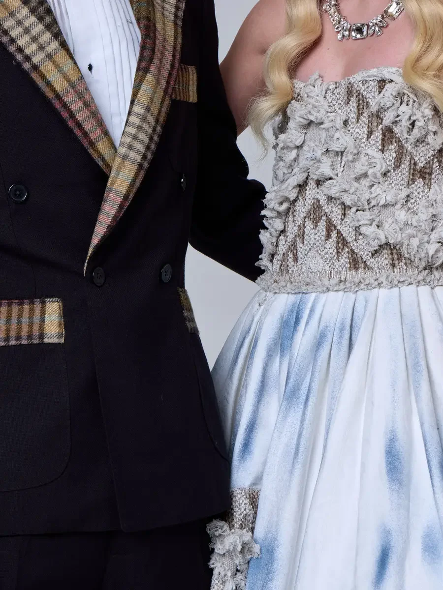 JUS10H 2025 New York Bridal Fashion Week, detail of black double-breasted suit with plaid lapels and pocket trim alongside ice-blue tie-dye ball gown with dimensional lace bodice and smocked waist, photographed by Scott Parker Photo