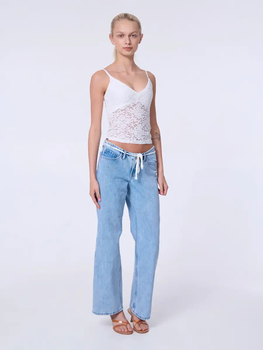 Model portfolio development session, commercial look, white lace crop camisole top and low-rise light wash wide-leg jeans with white drawstring detail, full-length, facing camera, arms at sides, elongated posture, chin slightly lifted, tan strappy he