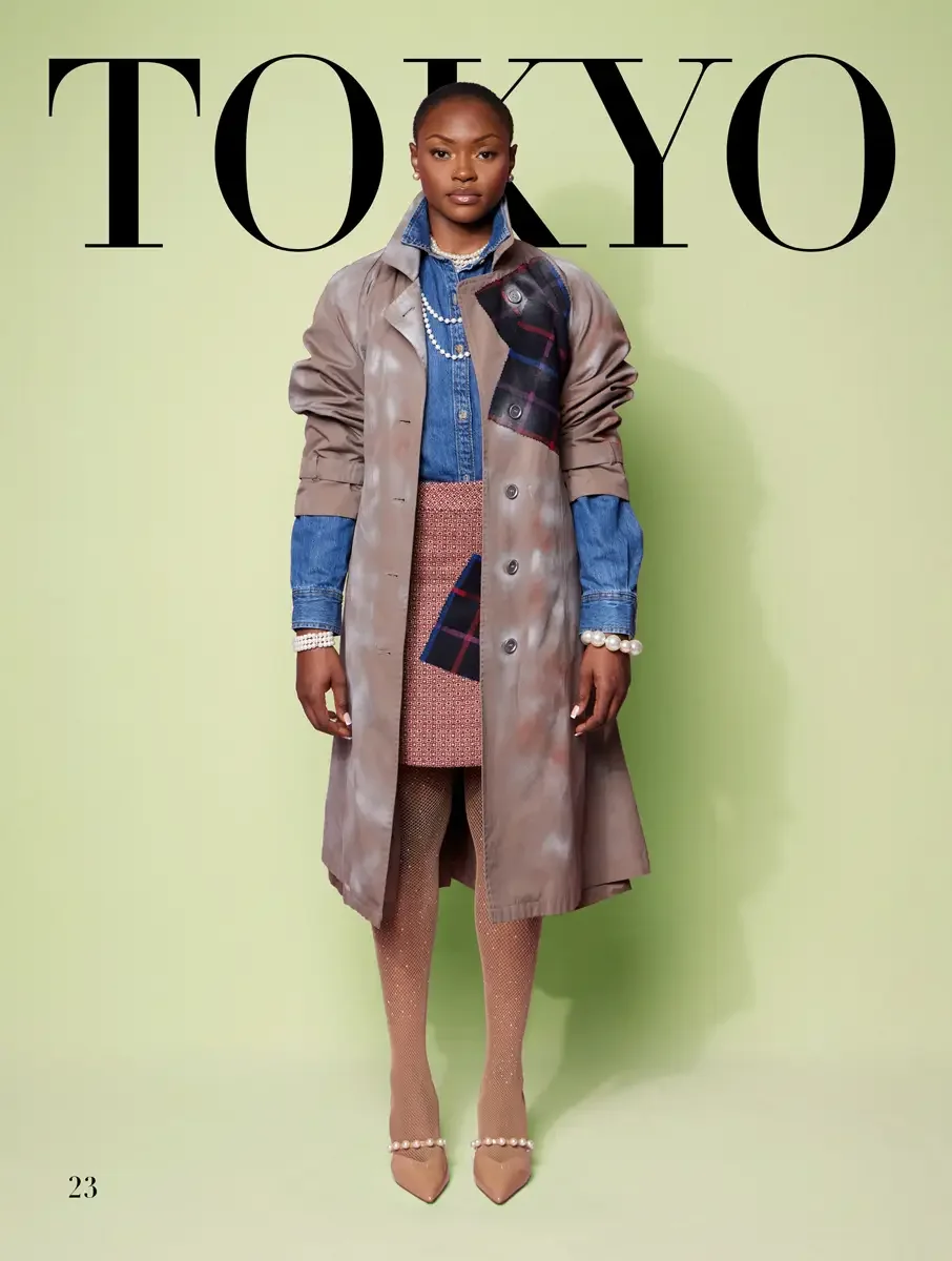 JUS10H 2025 Tokyo lookbook, tie-dye taupe trench coat with navy tartan patch over denim shirt and pink geometric mini skirt with fishnet tights and pearl strap heels, sage green background, photographed by Scott Parker Photo for the Tokyo Fashion Cou
