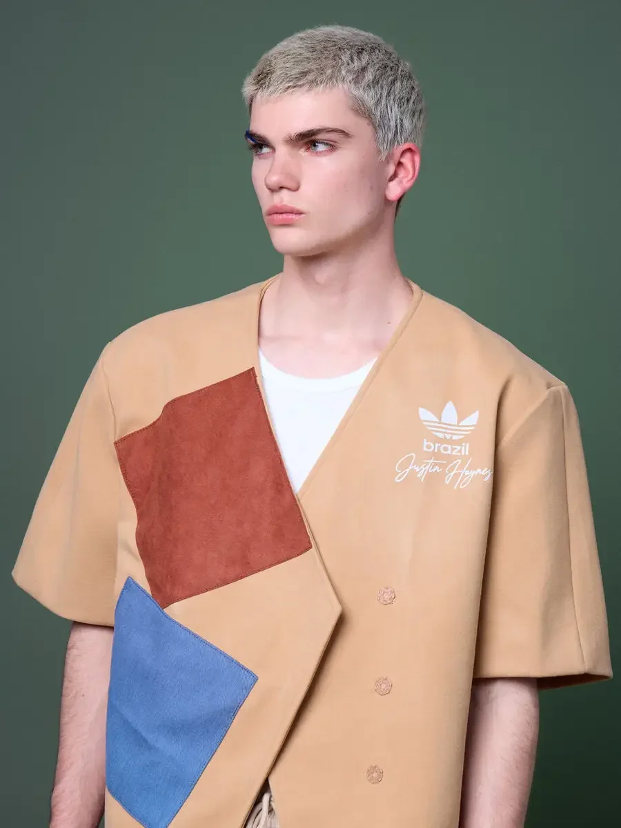 JUS10H x Adidas Brasil campaign, close editorial portrait, tan patchwork short-sleeve vest with terracotta and blue suede panels and Adidas Brasil Justin Haynes trefoil logo, blue graphic eyebrow detail, forest green background, photographed by Scott
