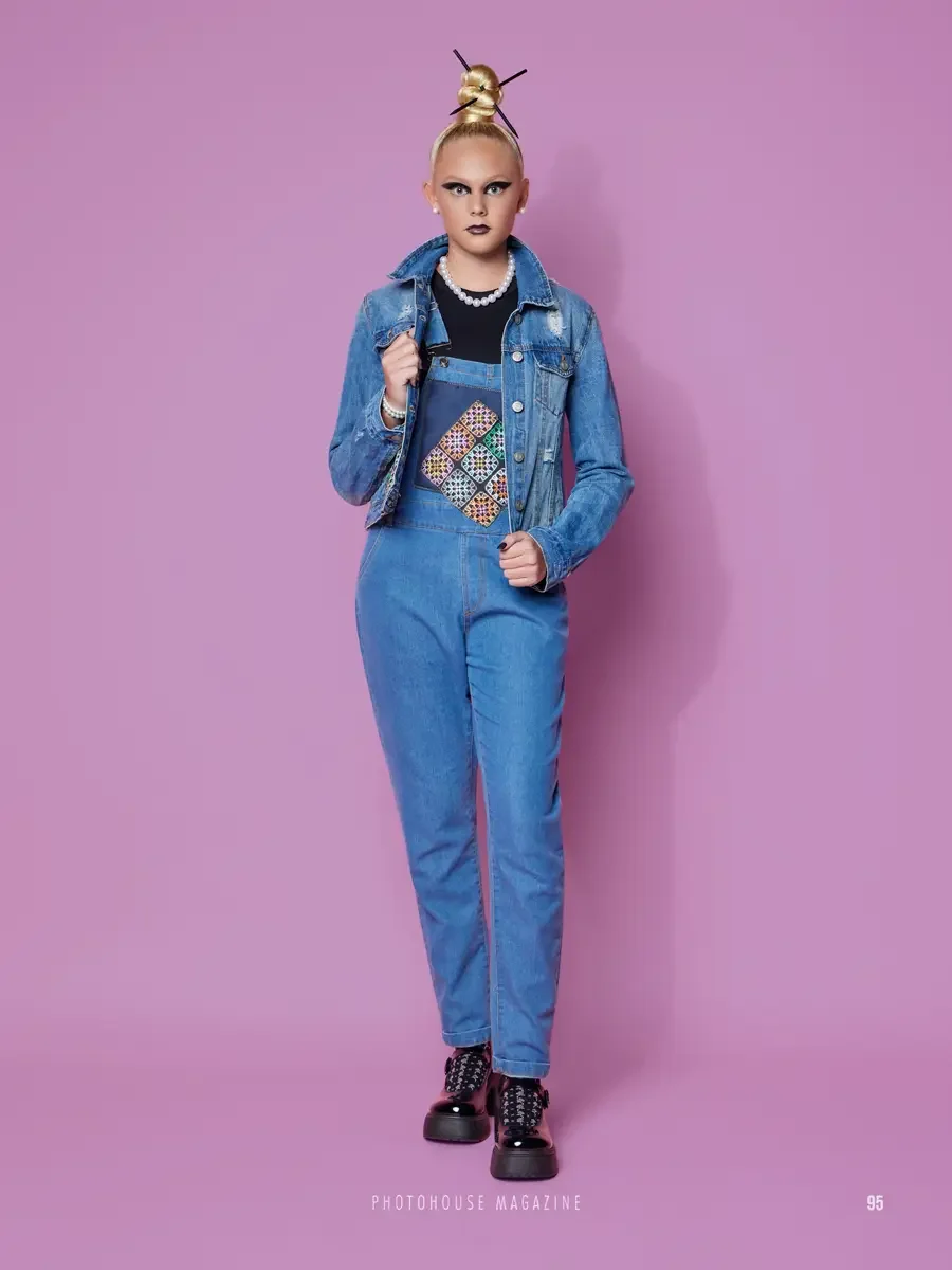 JUS10H 2025 Photohouse Magazine feature, model in light blue denim overalls with multicolor embroidered patchwork bib panel over cropped denim jacket and black tee, pearl necklace, platform lug-sole boots, lavender background, photographed by Scott P