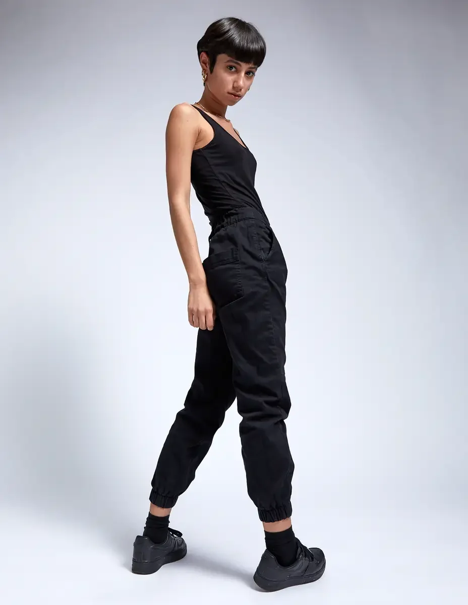 Eloissa, full-length dynamic pose, black tank and black cargo jogger pants, gold chain necklace, East Williamsburg studio test shoot, makeup by Schanica Pickens, photographed by Scott Parker Photo