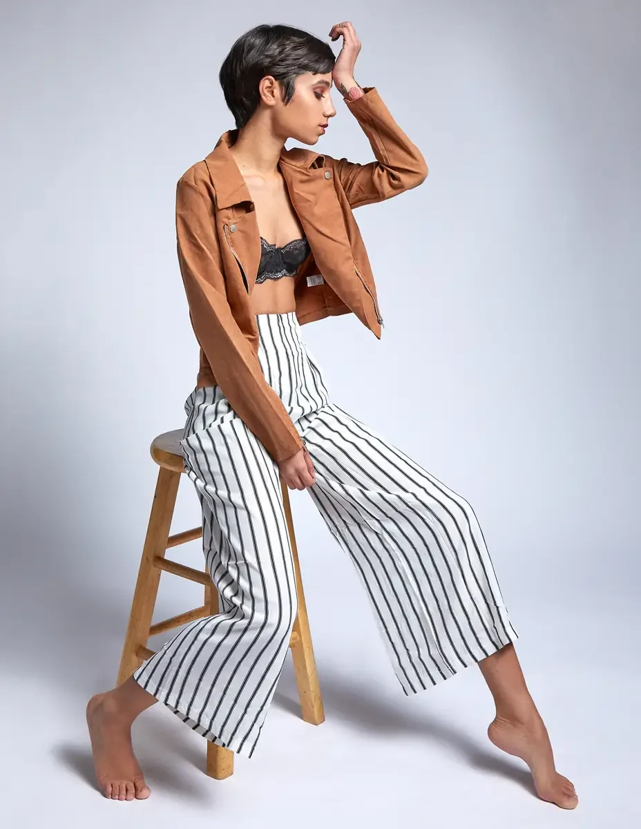 Eloissa, three-quarter profile, hand raised, tan suede jacket and striped wide-leg trousers, floral wrist tattoo, studio stool, East Williamsburg studio test shoot, makeup by Schanica Pickens, photographed by Scott Parker Photo