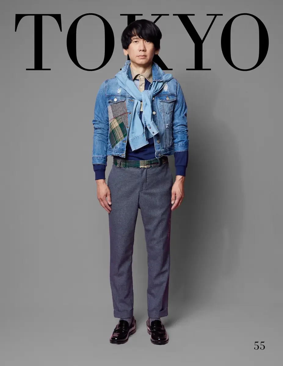 JUS10H 2025 Tokyo lookbook, a male model wearing a distressed light-wash denim trucker jacket with mixed plaid and tweed patchwork panels, layered over a navy crewneck sweater and a tan button-down shirt, with a light blue denim scarf tied at the nec