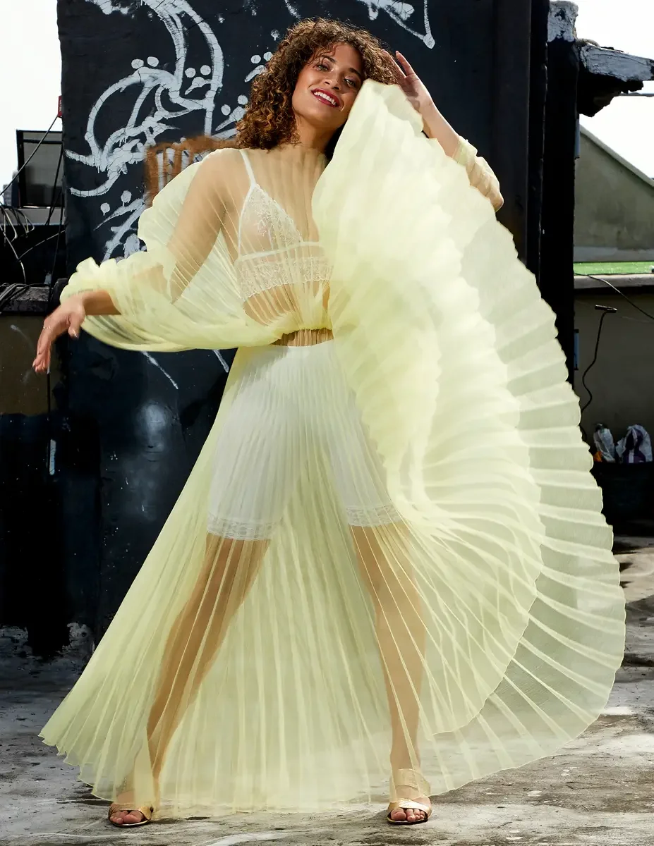 Fashion test shoot, model Ireland T in J'Amemme yellow pleated sheer gown in motion, Taro Collection earrings, graffiti wall backdrop, East Village rooftop, New York City, styling by Matsine Stinson, makeup by Stefani Paige Vivian, photographed by Sc