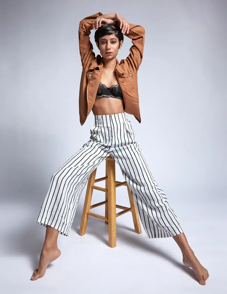 Eloissa, arms raised, white and black striped high-waisted wide-leg trousers, tan suede cropped jacket, black lace bralette, studio stool, East Williamsburg studio test shoot, makeup by Schanica Pickens, photographed by Scott Parker Photo