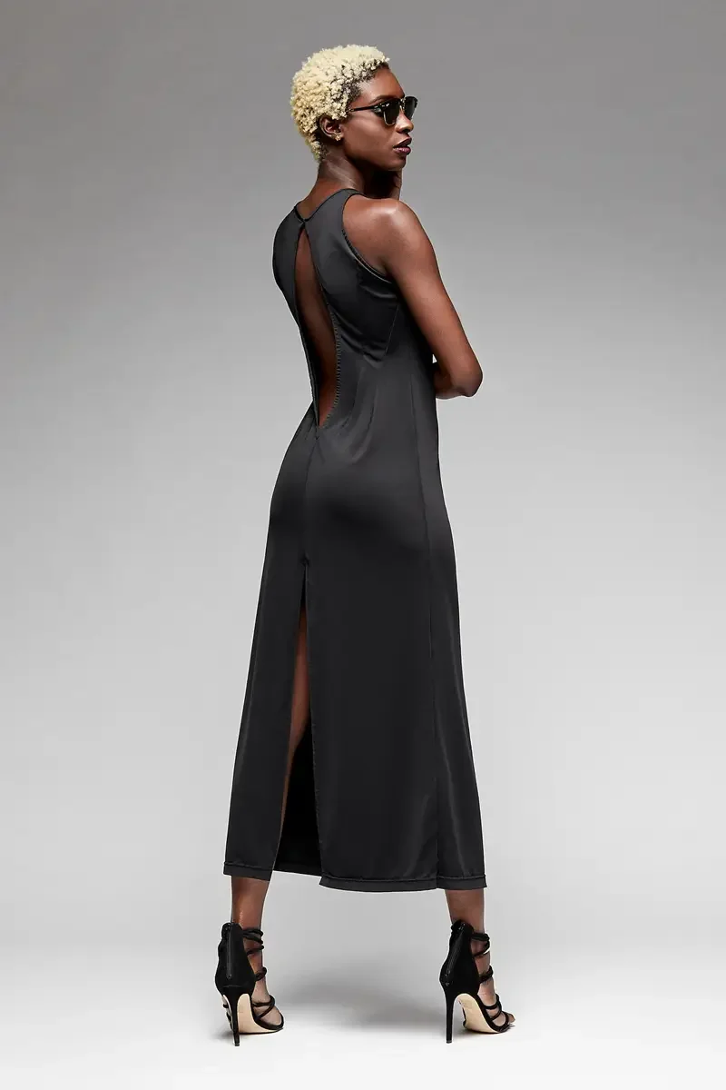 Minika Ko lookbook, black sleeveless jumpsuit, three-quarter back view, open back with narrow strap detail, side slit at hem, smooth synthetic fabric, dark sunglasses, photographed by Scott Parker Photo

