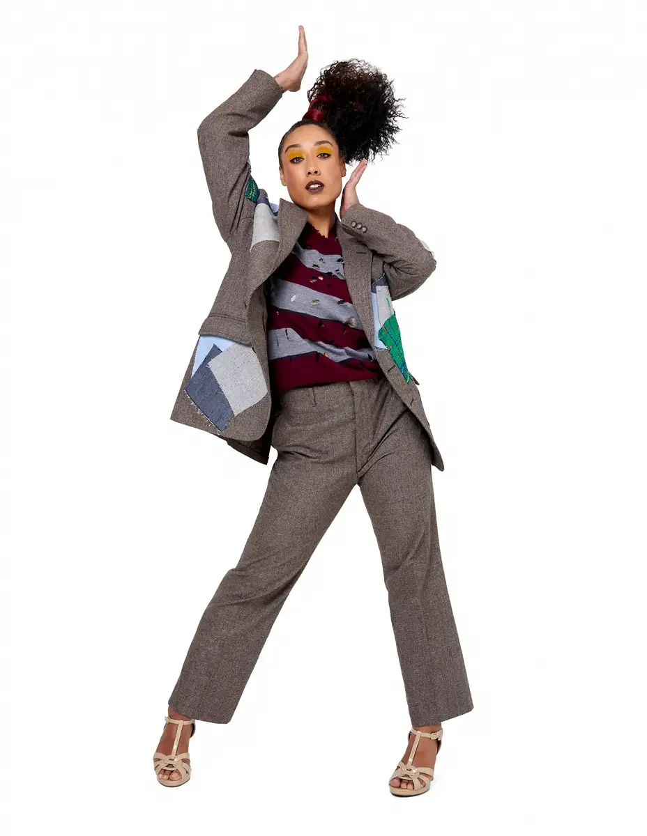 Model portfolio development session, high fashion editorial look, oversized heathered blazer with mixed fabric appliqué panels over burgundy and heather grey destroyed-knit stripe sweater with raw-edge sleeves, straight-leg heathered trousers, nude t
