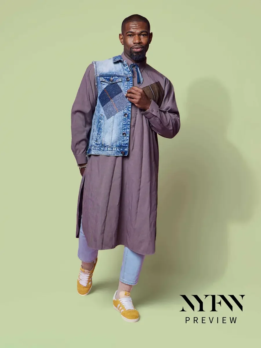 JUS10H 2025 promotional image, model in mauve longline shirt-dress with patchwork denim vest carried over one arm, light blue trousers and yellow sneakers, sage green background, photographed by Scott Parker Photo