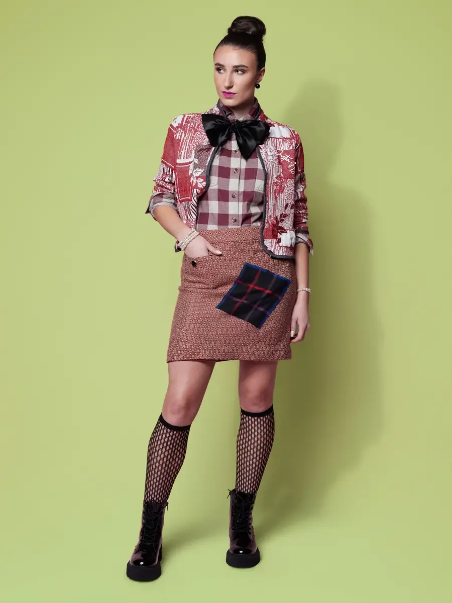 JUS10H 2025 Nylon Japan feature, model in red and white toile cropped jacket over burgundy plaid shirt with black oversized bow, rose tweed mini skirt with navy tartan patchwork panel, fishnet knee socks and black platform combat boots, sage green ba
