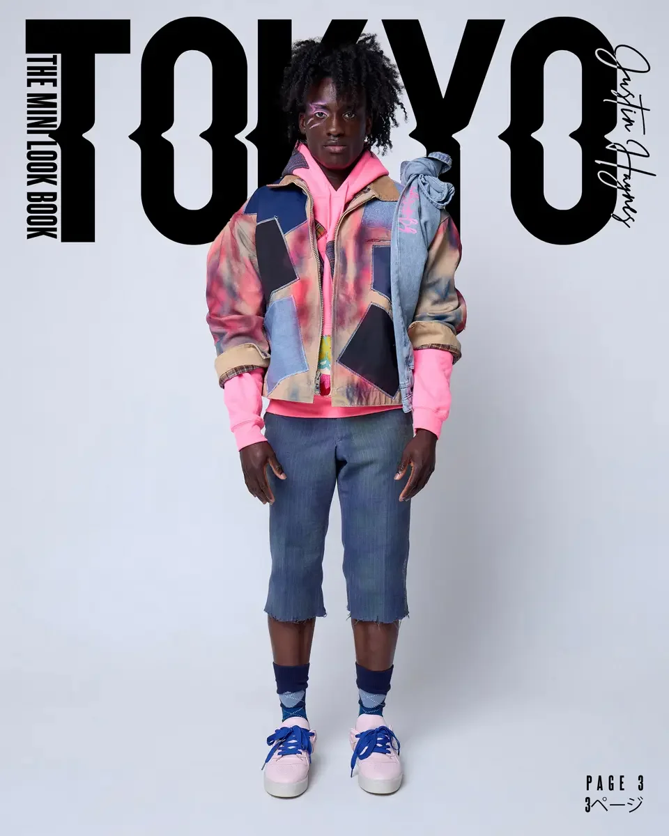 A person with dark skin, curly black hair, and a serious expression, dressed in colorful, layered clothing, standing in front of a white background with large black text that reads "TOKYO" and smaller text "The Min Look Book" and "Katia Hanys."