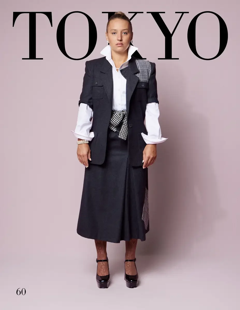 JUS10H 2025 Tokyo lookbook, a female model wearing a charcoal gray wool sleeveless blazer vest with a houndstooth patchwork panel at the shoulder and a houndstooth bow at the waist, over a white button-down shirt with wide cuffs, paired with a charco