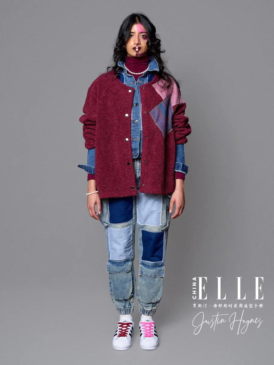 Model wearing a layered outfit with a red and pink oversized jacket, denim shirt, patchwork jeans, and white sneakers with red and pink laces, standing against a gray background for Elle China.
