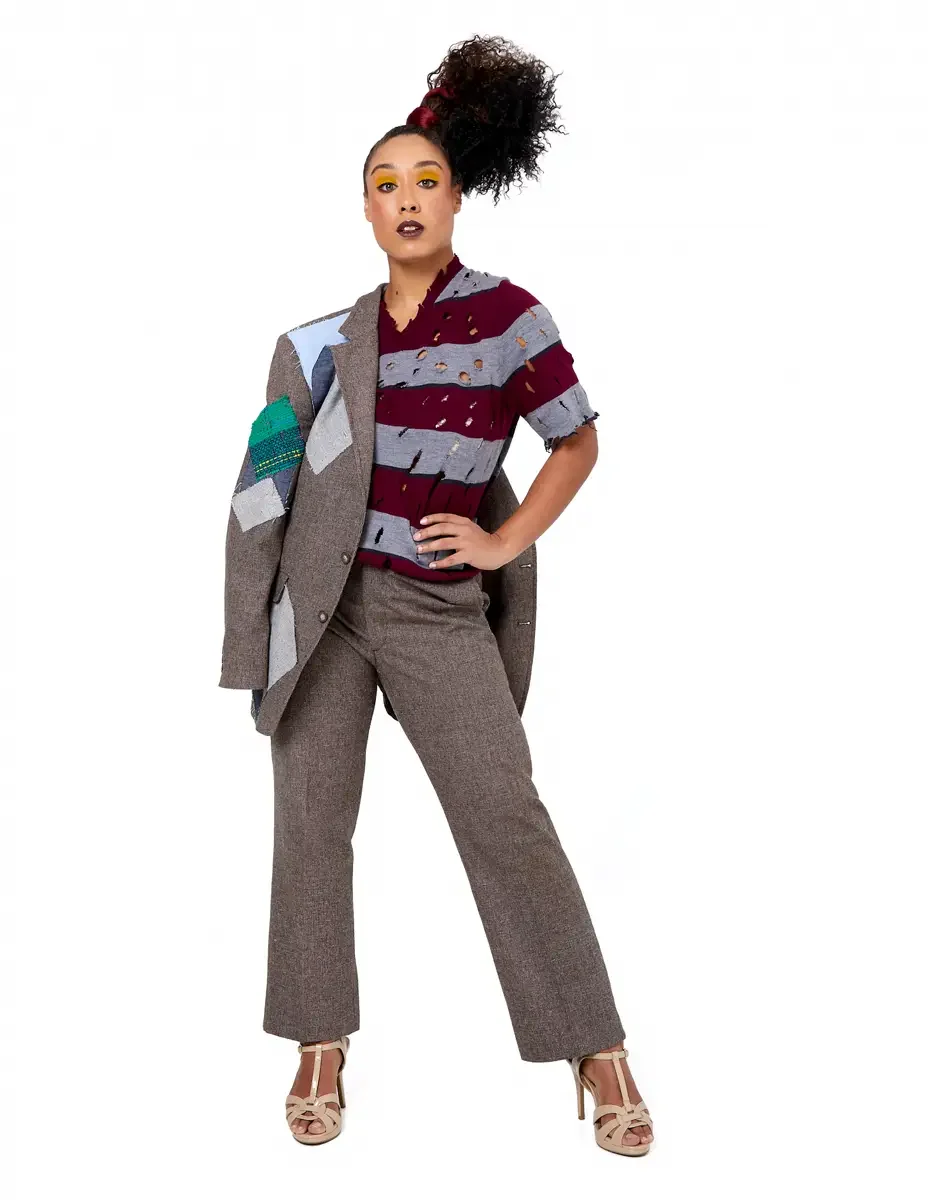 Model portfolio development session, high fashion editorial look, burgundy and heather grey destroyed-knit stripe sweater with raw-edge cutout sleeves, straight-leg heathered trousers, nude t-strap heels, blazer removed, full-length, hand on hip, dir