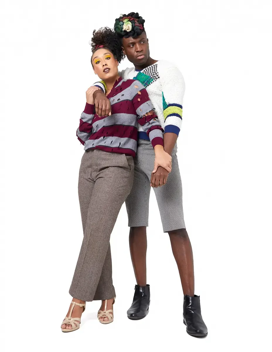 Model portfolio development session, high fashion editorial look, two models leaning into each other, woman in burgundy and heather grey destroyed-knit stripe sweater and straight-leg heathered trousers, man in white patchwork bouclé knit sweater and