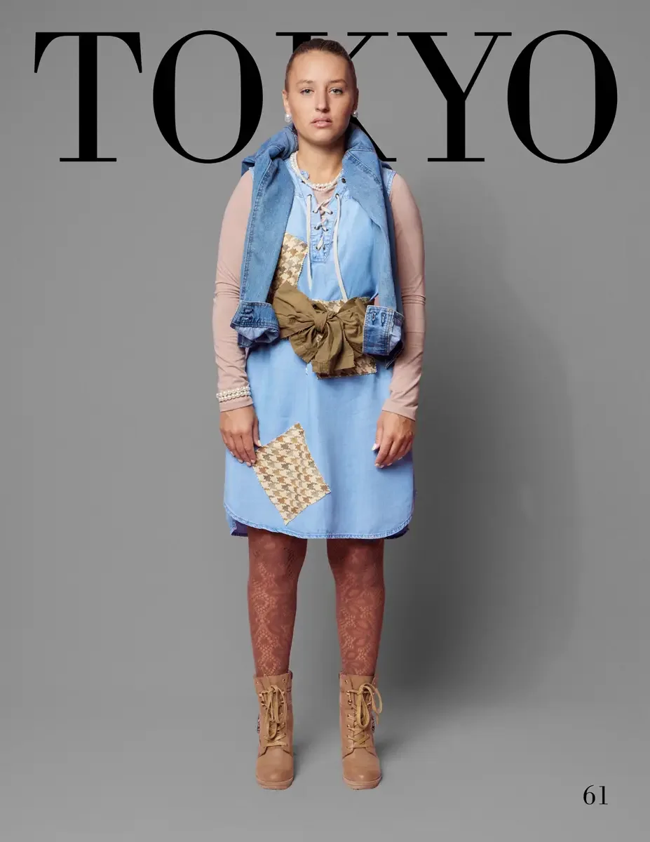 JUS10H 2025 Tokyo lookbook, a female model wearing a light blue sleeveless denim vest layered over a light blue lace-up denim shift dress with a tan and cream houndstooth patchwork panel, cinched with a large olive military bow belt, over a blush pin