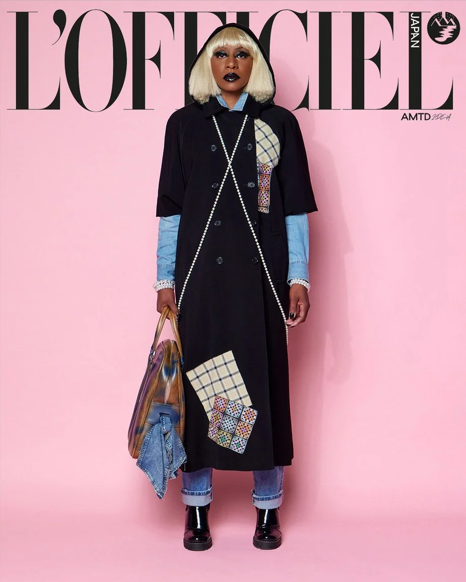 

JUS10H Tokyo Remote Collection NYFW 2025 — model Stewie in floor-length black hooded double-breasted coat with plaid and multicolor mosaic embroidered patchwork appliqué, light-wash denim shirt underlayer, cuffed jeans, carrying an iridescent overs