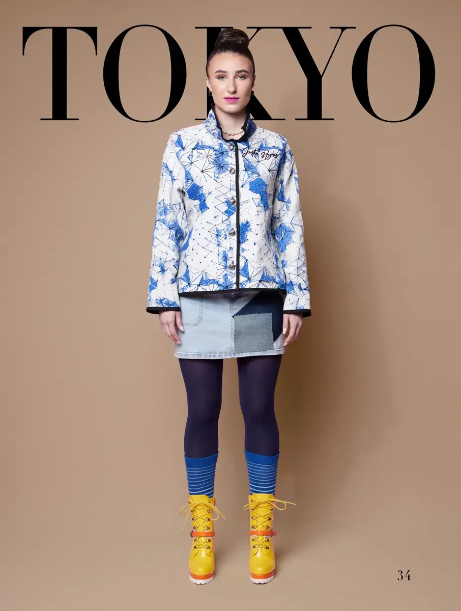 JUS10H 2025 Tokyo lookbook, a model wearing a white and cobalt blue geometric print structured jacket with black trim and a script logo, a patchwork light-wash denim mini skirt, navy tights, blue-striped ribbed socks, and bright yellow lace-up platfo