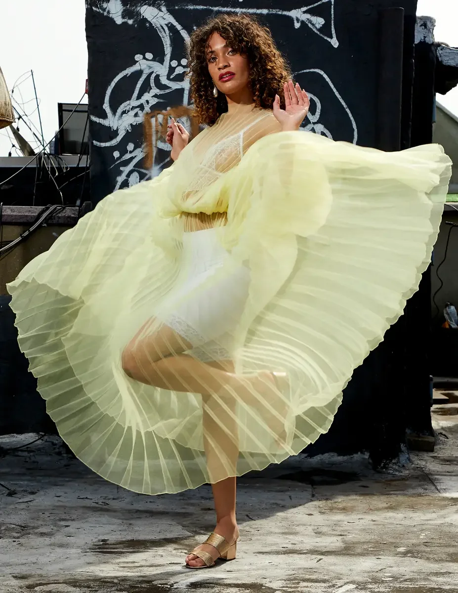 Fashion test shoot, model Ireland T in J'Amemme yellow pleated sheer gown, skirt lifted and spreading wide, graffiti wall backdrop, East Village rooftop, New York City, styling by Matsine Stinson, makeup by Stefani Paige Vivian, photographed by Scott
