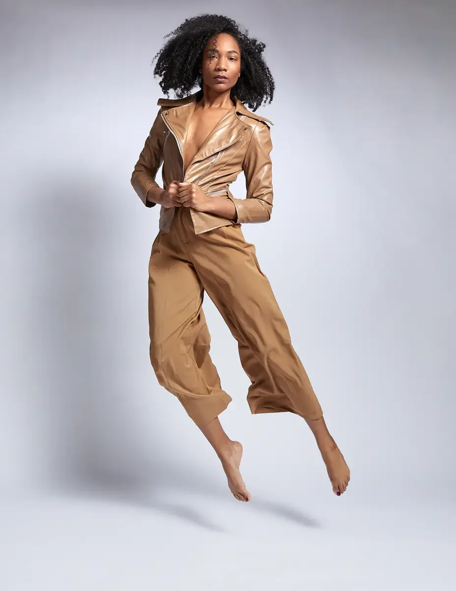 Arielle Chambers, camel patent leather moto jacket and wide-leg trousers, direct gaze, jumping, East Williamsburg studio test shoot, makeup by Schanica Pickens, photographed by Scott Parker Photo