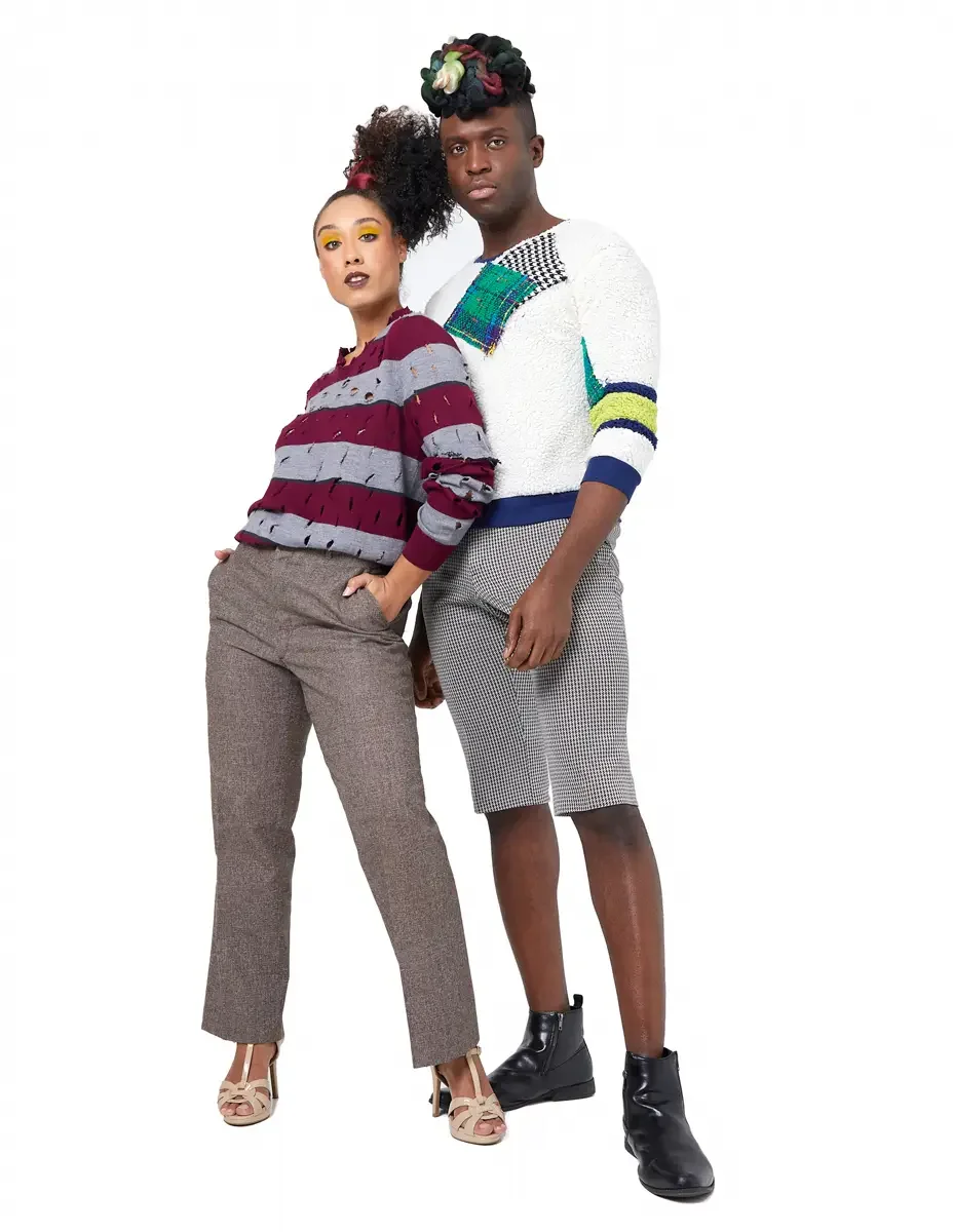Model portfolio development session, high fashion editorial look, two models standing together, woman in burgundy and heather grey destroyed-knit stripe sweater and straight-leg heathered trousers, man in white patchwork bouclé knit sweater with houn