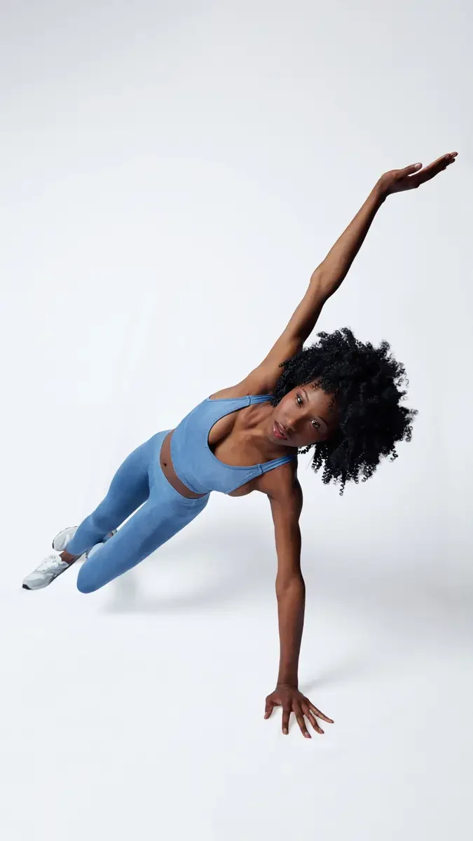 Model portfolio development session, commercial athletic look, blue sports bra and leggings, extreme side-plank pose with arm extended, white background, photographed by Scott Parker Photo, New York