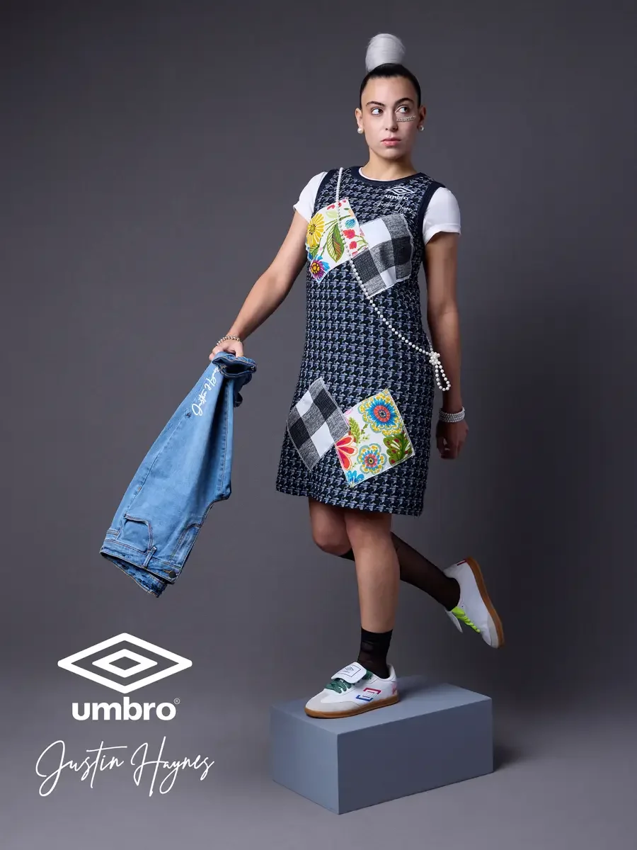 Fashion lifestyle photography for the Umbro France collection. Vanessa elevated and standing with a denim jacket carried low in a navy houndstooth sleeveless shift dress with diagonal floral and patchwork panels layered over a white t-shirt, styled b