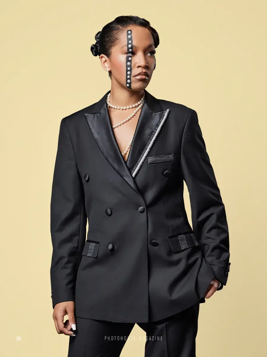 JUS10H 2025 Photohouse Magazine feature, model in black double-breasted satin blazer with textured patchwork lapel trim and welt pocket detail, layered pearl necklace, butter yellow background, photographed by Scott Parker Photo