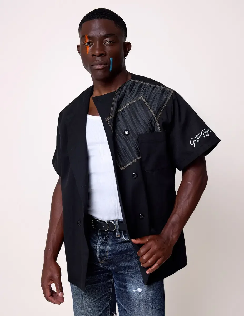 JUS10H Black Summer Jacket editorial, three-quarter portrait of male model in black double-breasted jacket with gray patchwork chest panel worn open over white tee, Justin Haynes signature on sleeve, dark jeans, white background, photographed by Scot