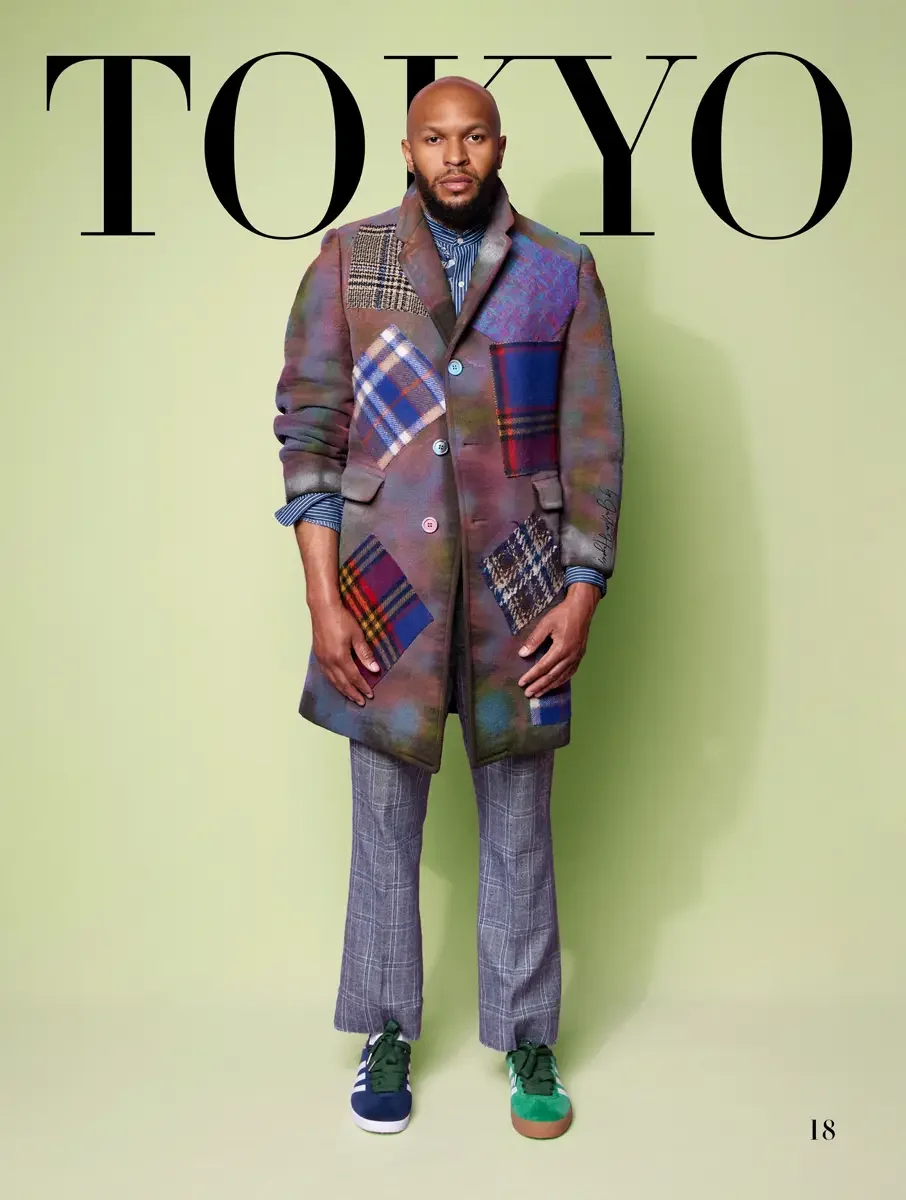 JUS10H 2025 Tokyo lookbook, tie-dye multicolor patchwork overcoat with tartan and plaid panels over striped shirt and glen plaid trousers with green Adidas sneakers, sage green background, photographed by Scott Parker Photo for the Tokyo Fashion Coun