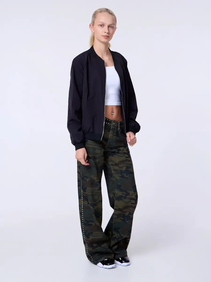 Model portfolio development session, commercial look, black bomber jacket open over white crop tank, low-rise studded camouflage wide-leg trousers with silver stud trim at waistband and side seam, full-length, slight turn to camera, arms relaxed, stu