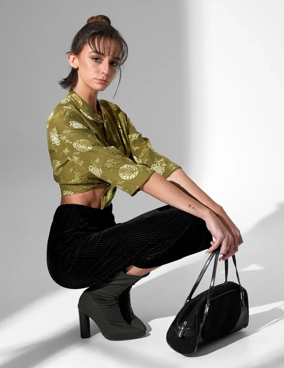 Macy, full length, crouching, olive green satin jacquard tied crop top with gold medallion print and frog closures, black wide-leg ribbed velvet culottes, olive green block-heel sock boots, black suede barrel bag, New York studio test shoot, photogra