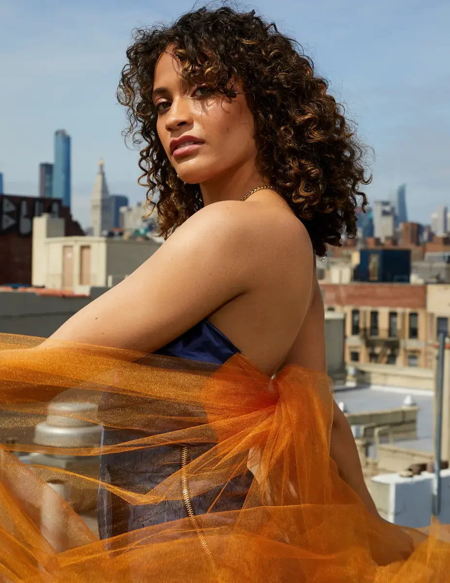 Fashion test shoot, three-quarter portrait of model Ireland T in Amy Page DeBlasio navy strapless top and textured blue wide-leg pants, orange tulle, Manhattan skyline, East Village rooftop, New York City, styling by Matsine Stinson, makeup by Stefan