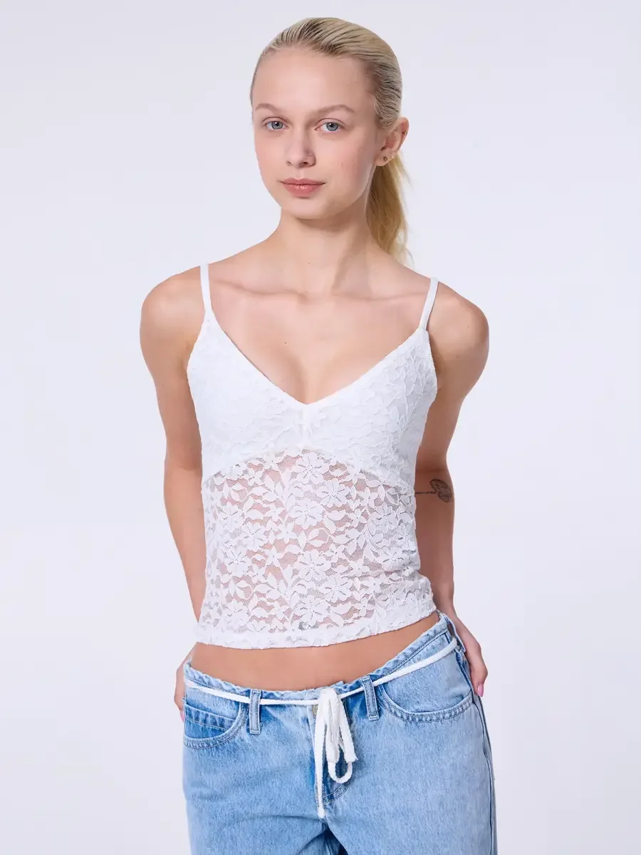 Model portfolio development session, commercial look, white lace crop camisole top with floral lace panel and low-rise light wash wide-leg jeans with white drawstring detail, three-quarter, facing camera, hands in back pockets, lace texture and sheer