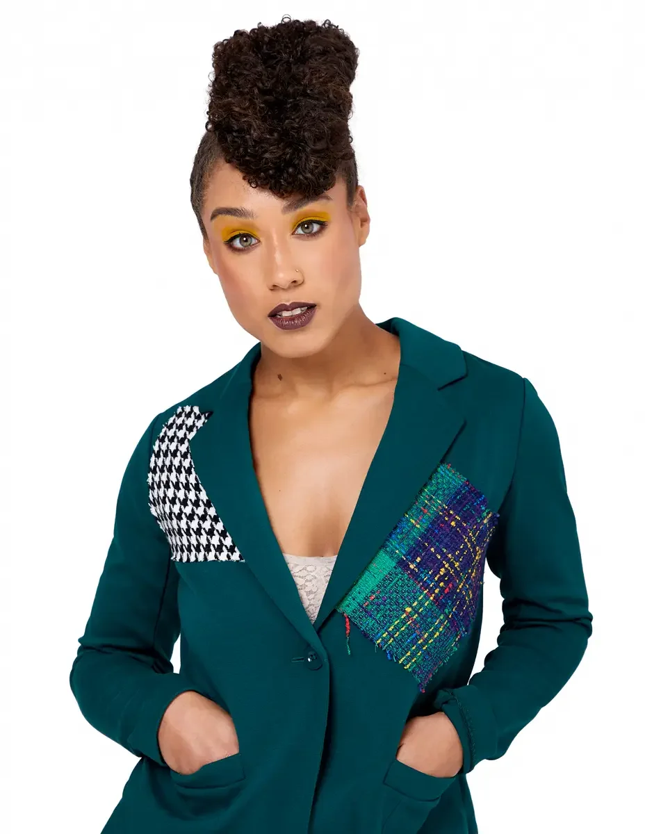 Model portfolio development session, high fashion editorial look, teal single-button blazer with houndstooth and multicolor tweed appliqué panels, three-quarter, hands in pockets, direct gaze, gold editorial eye makeup, dark lip, white background
