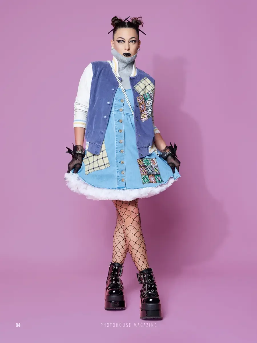 JUS10H 2025 Photohouse Magazine feature, model in periwinkle velvet varsity vest with tartan and multicolor embroidered patchwork panels over light blue denim button-front mini dress with fur hem trim, grey turtleneck, fishnet tights, and platform bo