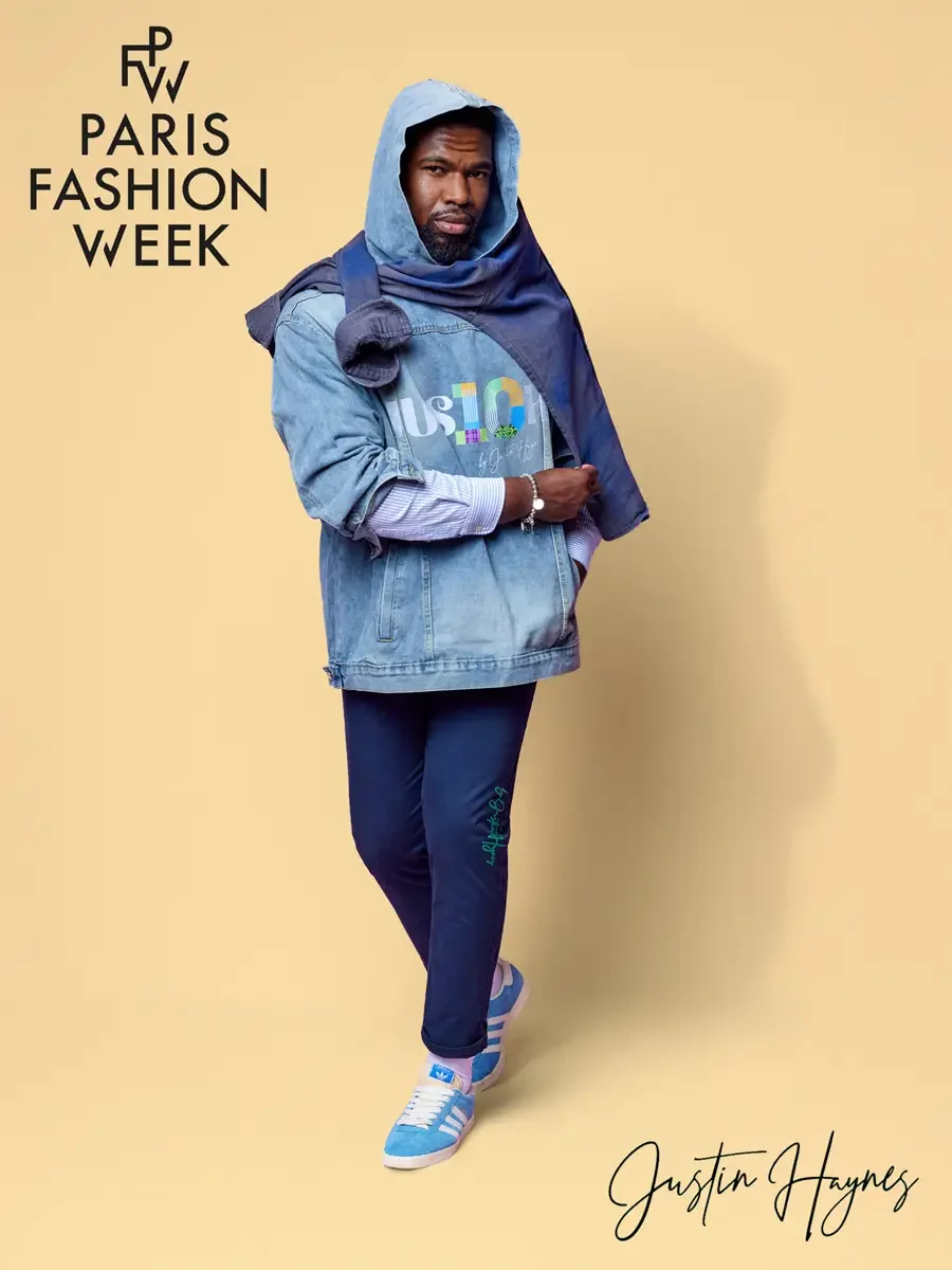 JUS10H 2025 promotional image, model in light wash JUS10H logo denim jacket layered over navy hoodie and striped shirt, navy JUS10H script trousers, sky blue sneakers, butter yellow background, photographed by Scott Parker Photo