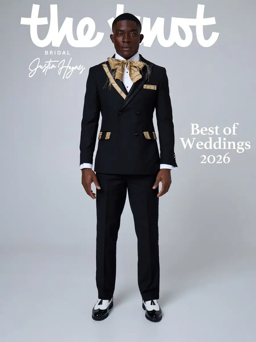 JUS10H 2025 The Knot Bridal feature, Justin Haynes Best of Weddings 2026 cover, black double-breasted suit with gold lapels, gold pocket trim, and oversized gold bow tie with feather detail, styled with black-and-white wingtip tasseled loafers, photo