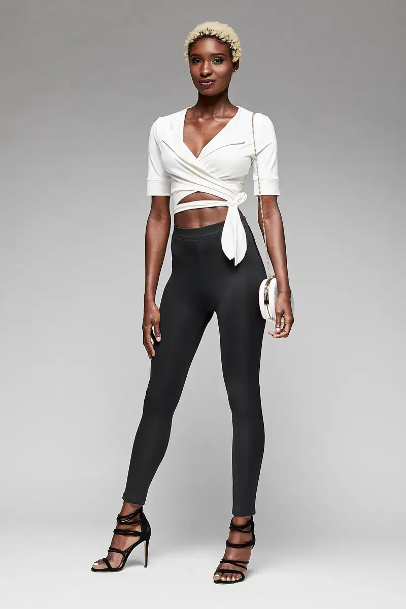 Minika Ko lookbook, black high-waist leggings and white wrap crop top, front view, deep V-neckline, wrap bodice with tie at waist, elbow-length sleeves, white circular crossbody bag, photographed by Scott Parker Photo