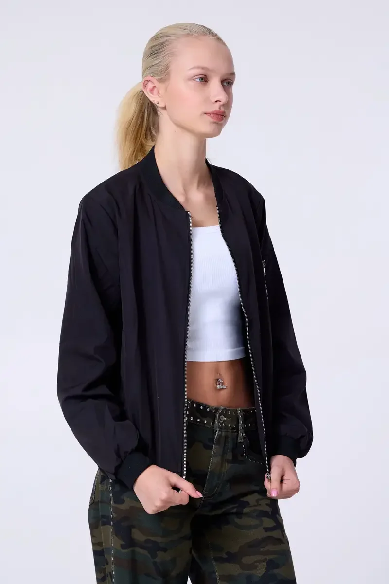 Model portfolio development session, commercial look, black bomber jacket open over white crop tank, low-rise studded camouflage wide-leg trousers with silver stud waistband detail, three-quarter, slight turn, gaze directed off-camera, hands at waist