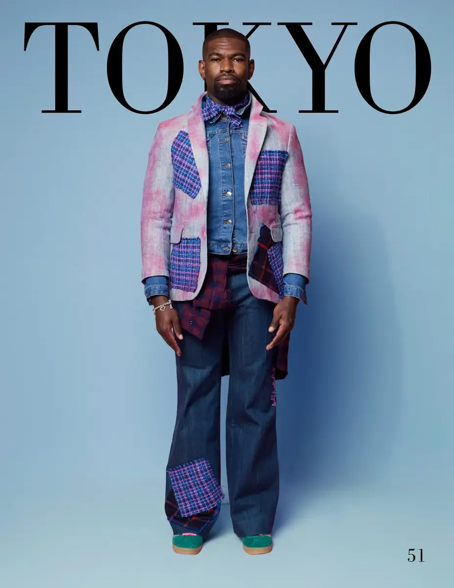 JUS10H 2025 Tokyo lookbook, a male model wearing a pink and gray acid-wash blazer with colorful pink and blue tweed patchwork panels and a plaid lining detail, layered over a denim trucker jacket and a burgundy plaid shirt, wide-leg dark indigo denim