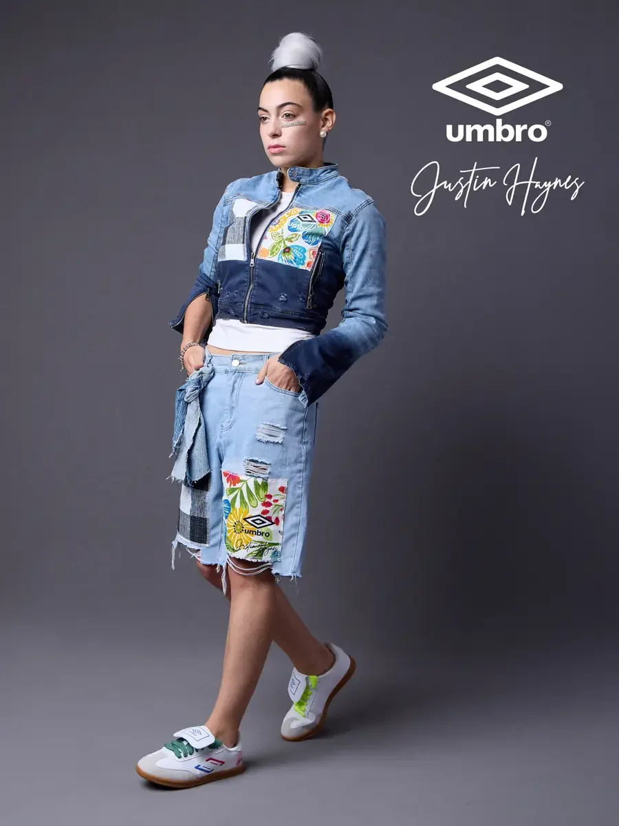 Fashion brand photography for the Umbro France collection. Vanessa in a walking stride with hands in pocket in a cropped two-tone denim moto jacket with floral patchwork panels and matching distressed denim bermuda shorts, styled by Justin Haynes, mo