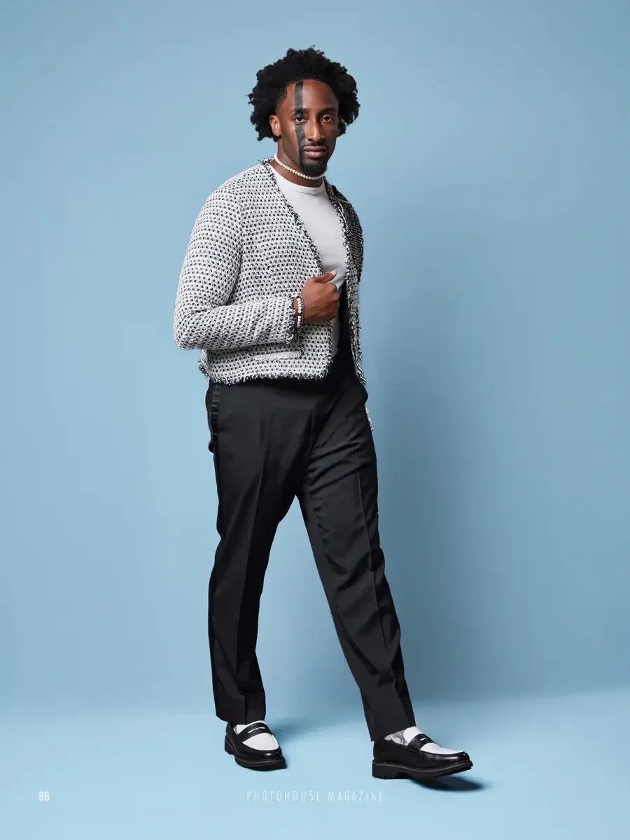 JUS10H 2025 Photohouse Magazine feature, model in white and black fringe-trimmed boucle cardigan over white turtleneck and black tailored trousers, pearl necklace, two-tone penny loafers, light blue background, photographed by Scott Parker Photo