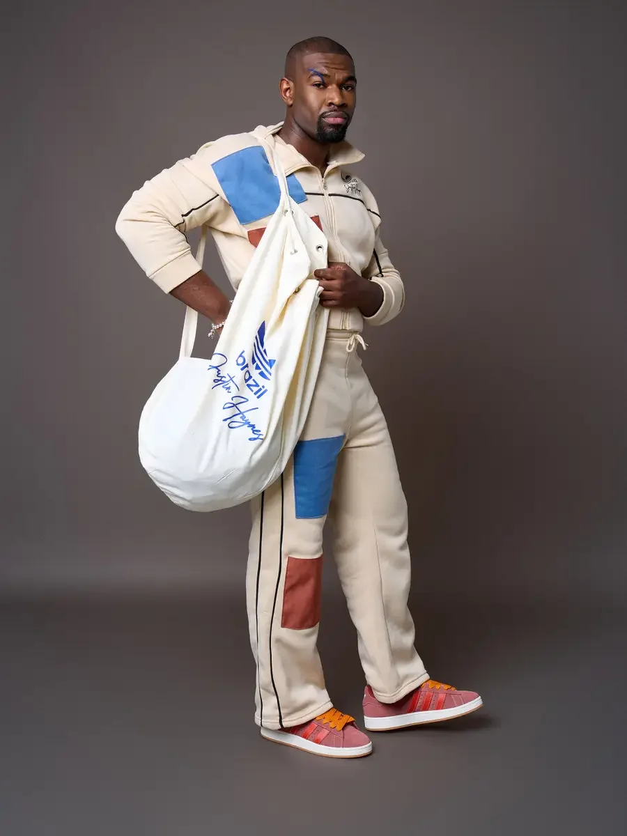 JUS10H x Adidas Brasil campaign, model standing with white JUS10H Adidas Brasil tote bag slung over shoulder, cream patchwork tracksuit with blue and terracotta suede panels and black piping, Adidas Campus 00s in pink suede with red stripes and orang